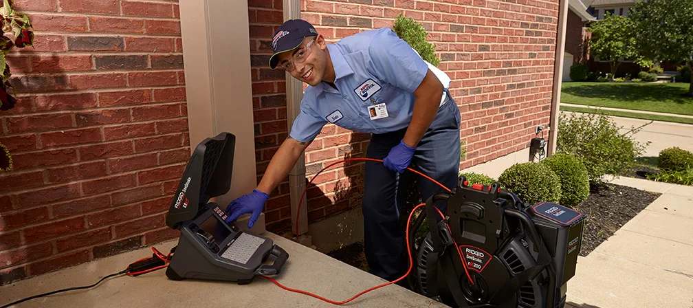 Roto-Rooter technician operating a drain inspection camera outside a home